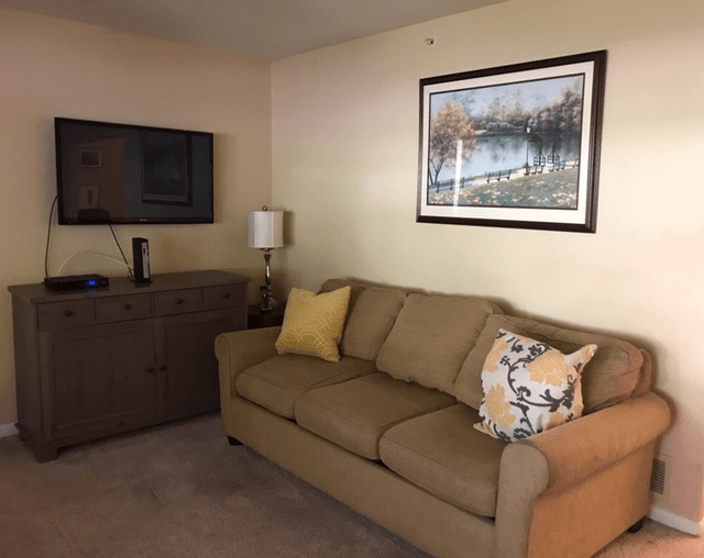 A cozy living room with a brown sofa, decorative pillows, a wall-mounted television, and artwork.