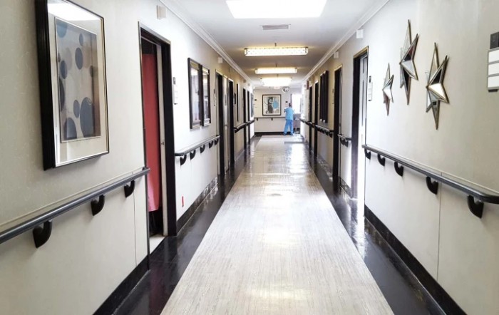 A hospital corridor with rooms on either side, featuring bright lighting and clean floors.