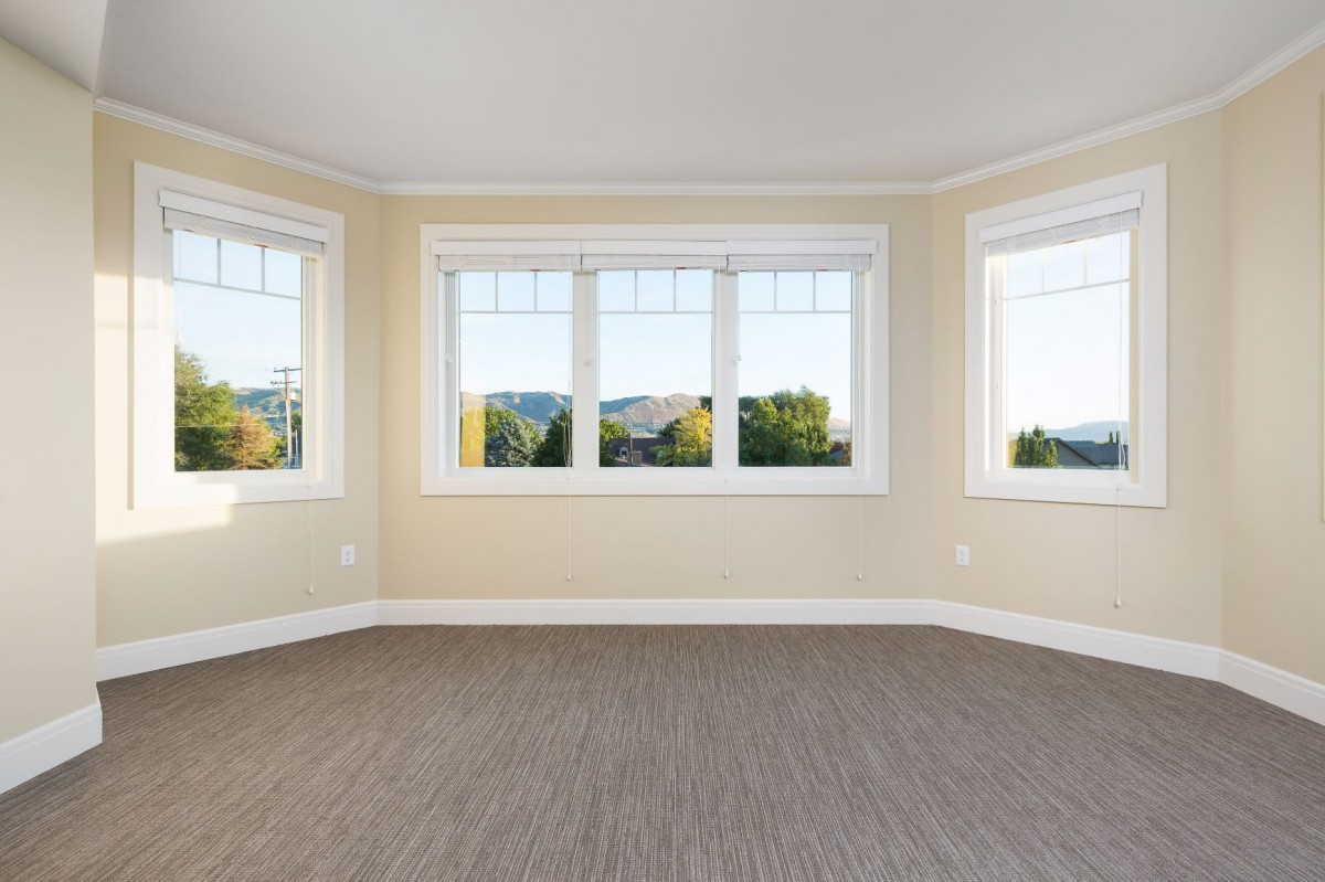 A spacious room with large windows offering a scenic view, featuring neutral-colored walls and carpeted flooring.