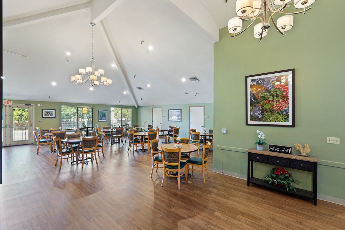 A spacious dining area with wooden floors, tables and chairs, adorned with chandeliers and wall art.