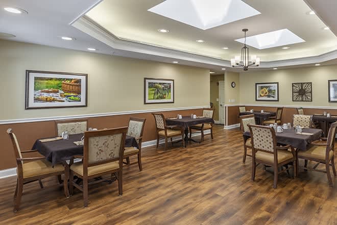 A well-lit dining room with wooden flooring and neatly arranged tables and chairs.