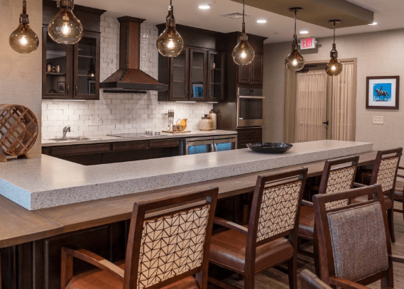 A modern kitchen with dark wood cabinets, pendant lighting, and a long countertop featuring bar stools.