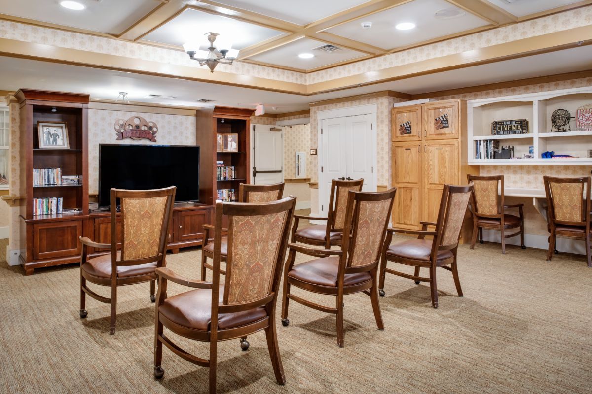A cozy meeting room with wooden chairs arranged in rows facing a television and bookshelf.