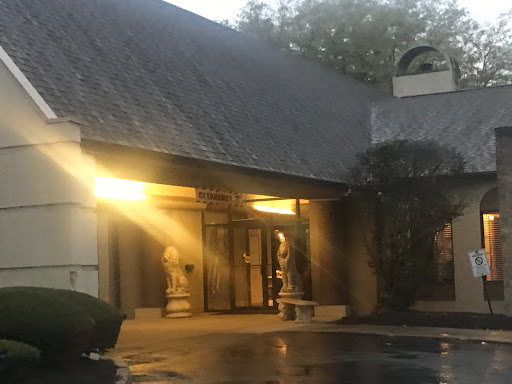 A tranquil evening view of a building entrance illuminated by warm light, featuring decorative statues on either side.
