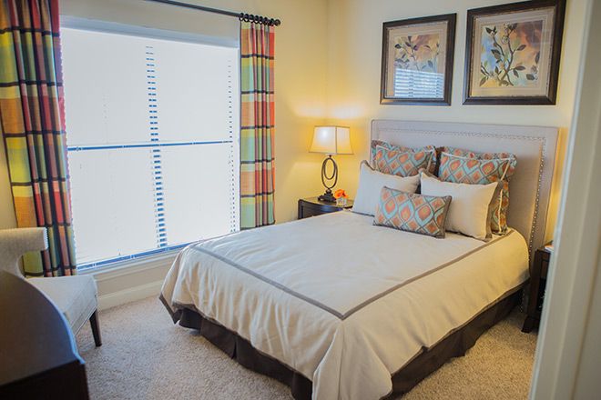A cozy and well-decorated bedroom with a neatly made bed, bedside lamp, and framed artwork on the walls.