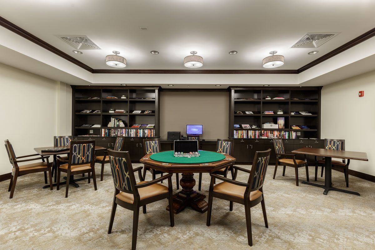 A cozy gaming room featuring a poker table surrounded by chairs and lined with bookshelves.