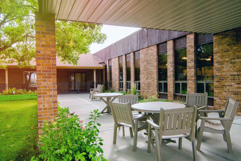 An outdoor patio area with tables and chairs adjacent to a brick building.