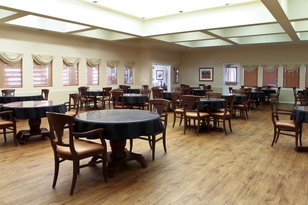 An empty dining room with multiple tables and chairs on a wooden floor.