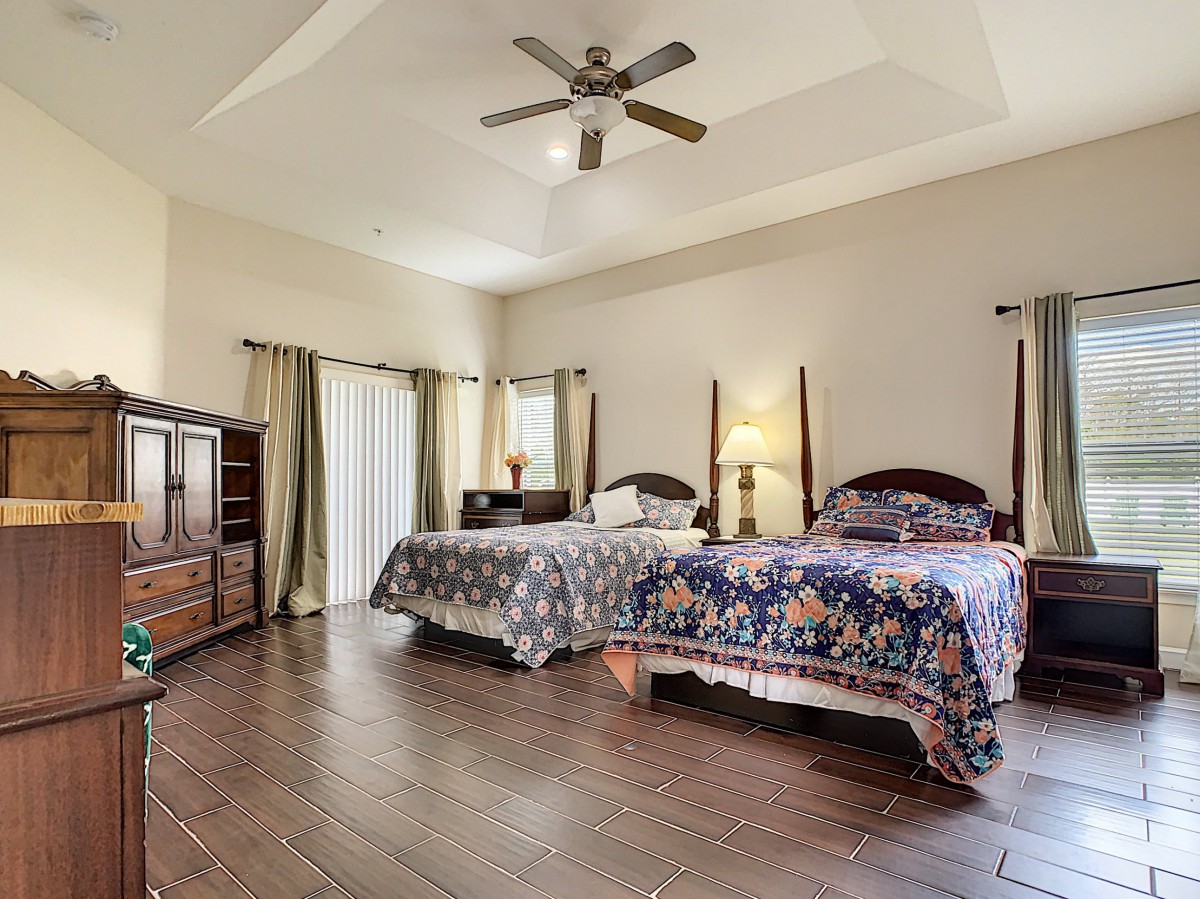 A spacious bedroom with two double beds, wooden floors, and a ceiling fan.
