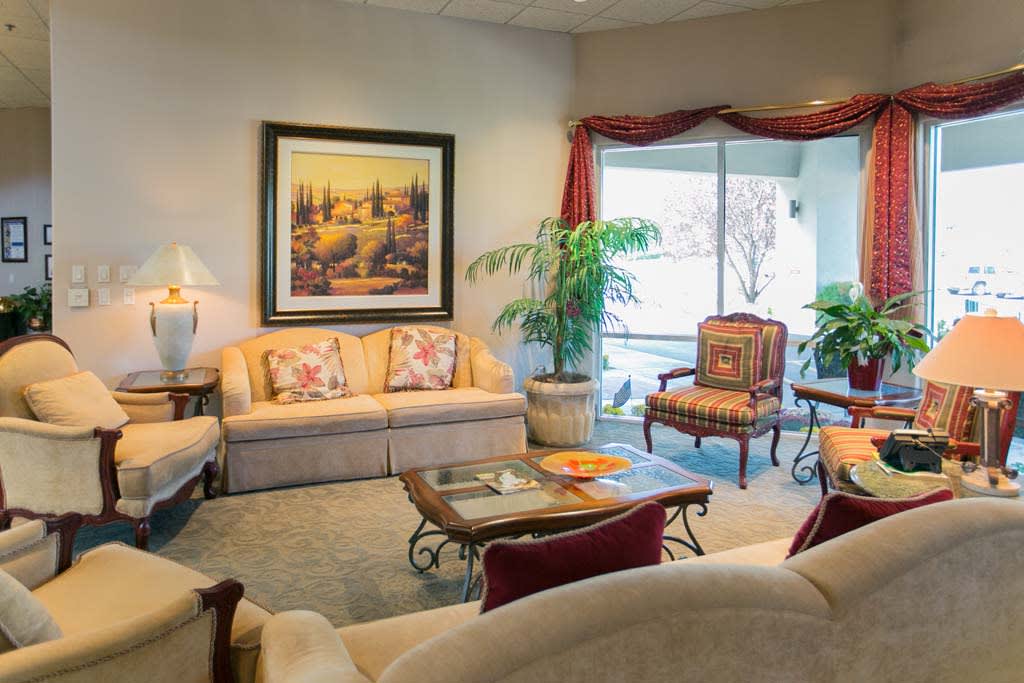A cozy living room featuring a beige sofa, armchairs, and a coffee table, complemented by a large painting and indoor plants.