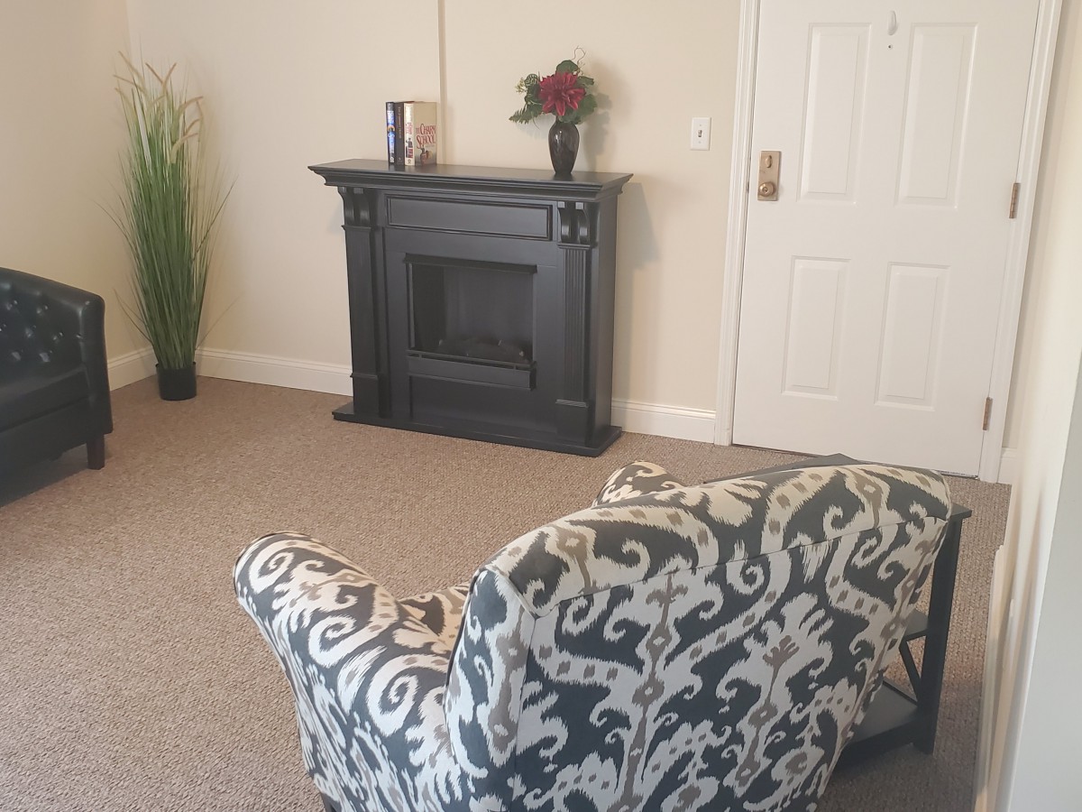 A cozy living room featuring a decorative black fireplace, an ornate patterned chair, and accent decor including a vase with flowers.