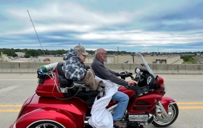 Two people riding a red trike motorcycle on a cloudy day.