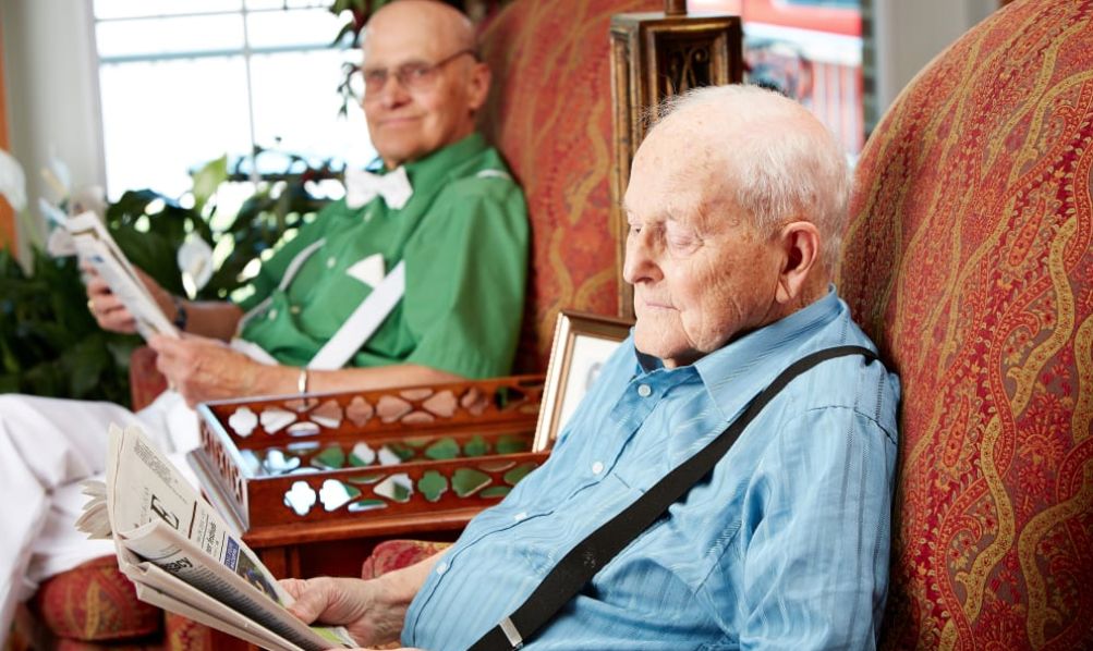Two elderly men relaxing indoors, one reading a newspaper.