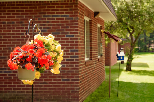 A vibrant display of flowers hangs beside a brick house, complemented by a birdhouse in the garden.