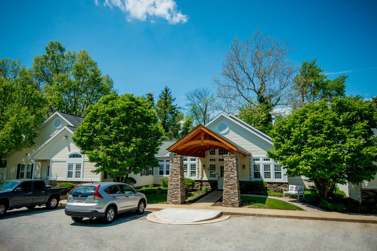 A picturesque house with a welcoming entrance, surrounded by lush greenery and parked car under a clear blue sky.