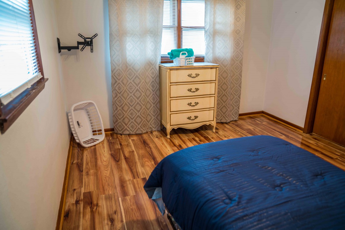 A cozy bedroom with a wooden floor, featuring a bed with blue bedding and a vintage dresser by the window.
