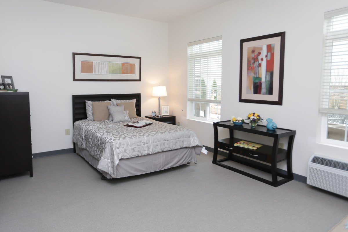 A modern, minimalist bedroom with a neatly made bed, contemporary artwork on the walls, and a bedside lamp and table.