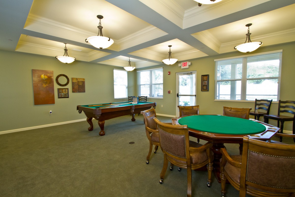 A well-appointed game room featuring a pool table and a card table with chairs, illuminated by ceiling lights.