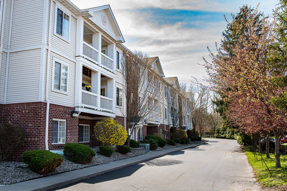 A view of a residential apartment building with white exteriors and surrounding trees.