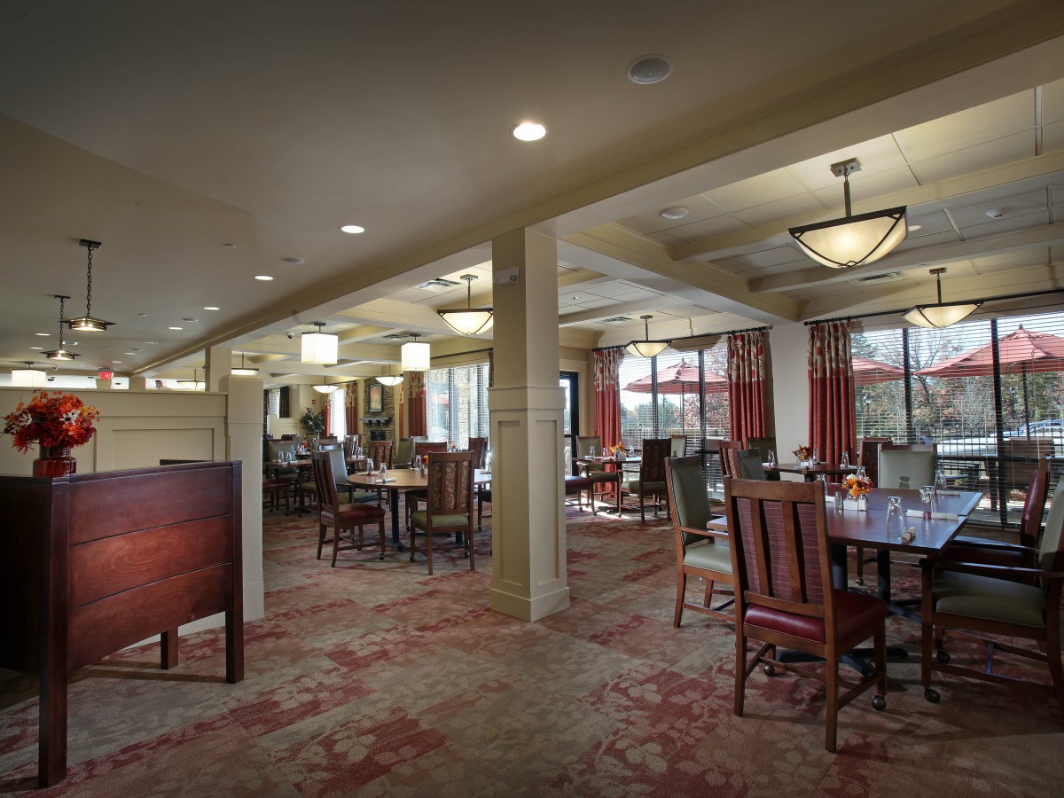 A cozy dining room with elegant tables and chairs, featuring warm lighting and a patterned carpet.