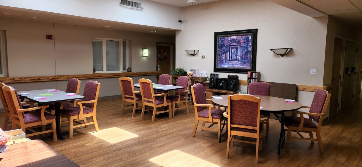 An empty dining room with several tables and chairs, featuring a framed artwork on the wall.