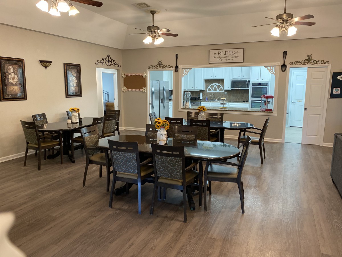 A cozy dining area with multiple tables and chairs, featuring a view into the kitchen and lit by ceiling fans.