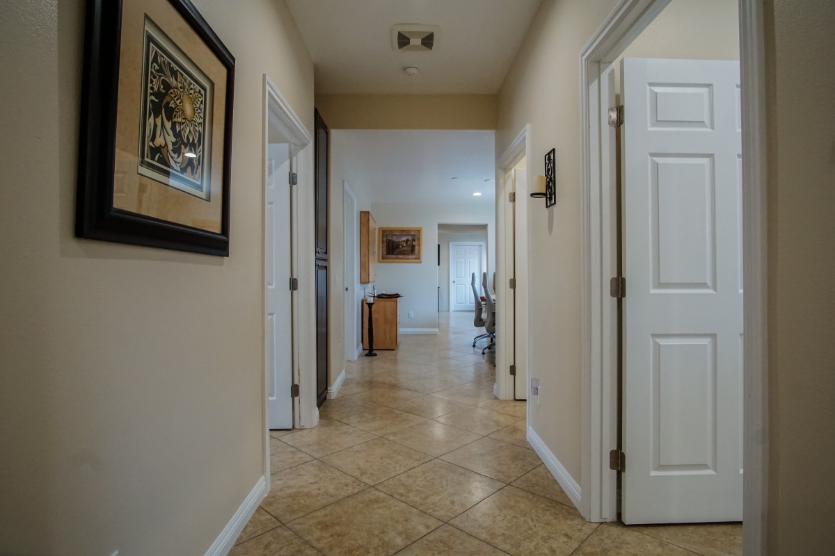 A view down a well-lit hallway with tile flooring and several doors leading to different rooms.
