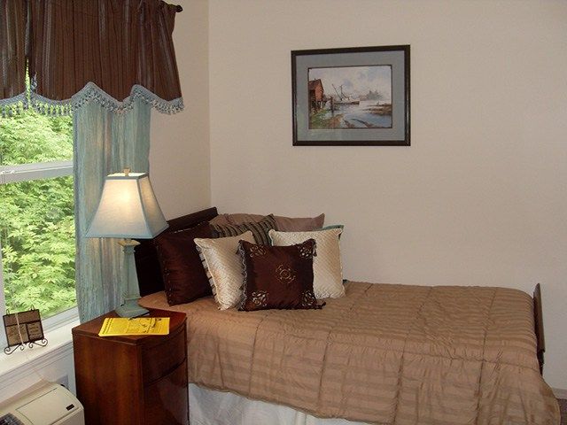 A cozy bedroom corner with a bed adorned with multiple pillows, a lamp on a side table, and curtains by the window.