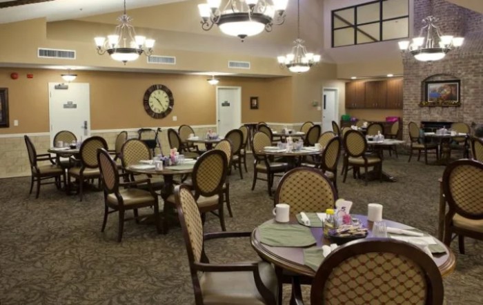 A well-lit dining area with round tables and elegant chairs, featuring chandeliers overhead.