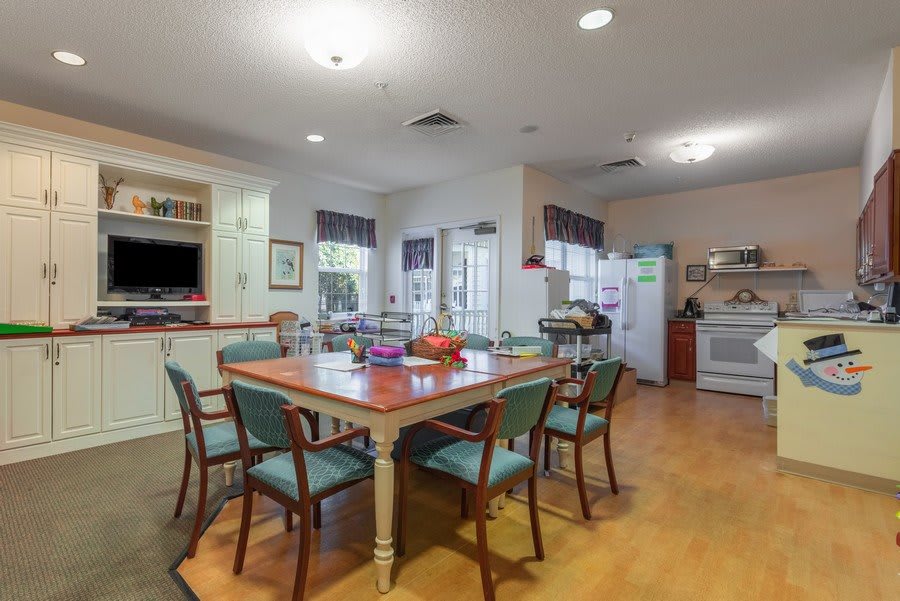 A well-lit dining and kitchen area with a large wooden table, surrounded by chairs, and modern kitchen appliances in the background.