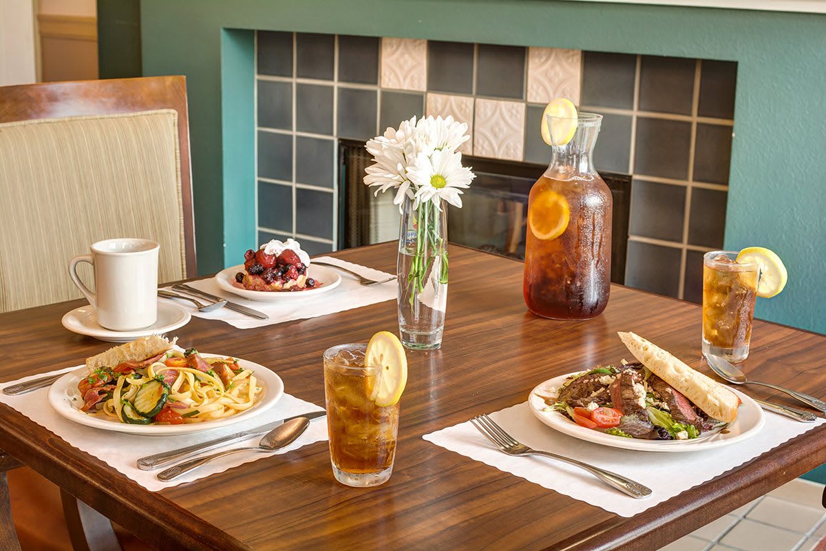 A dining table set with various dishes, including pasta and salad, accompanied by iced tea and a floral centerpiece.