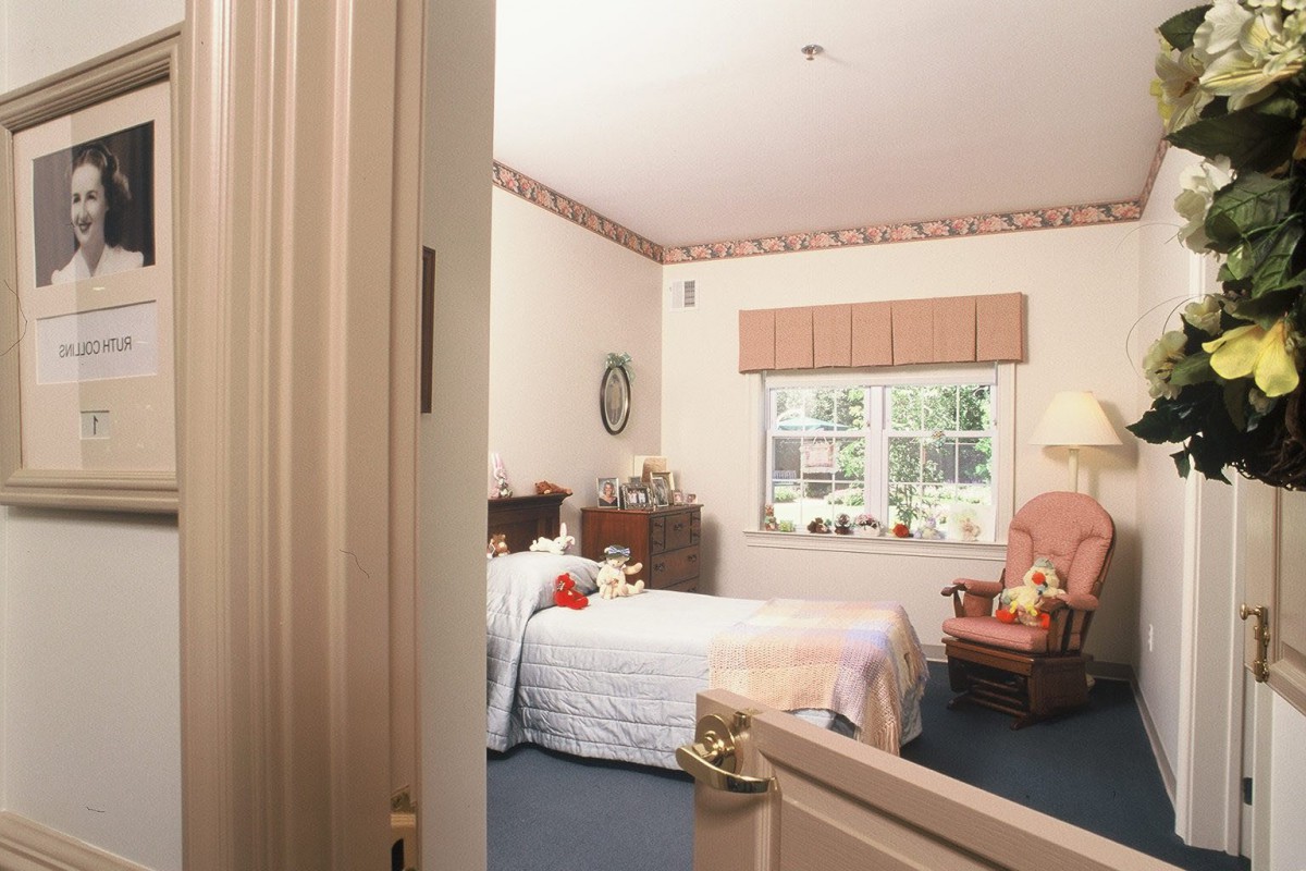 A cozy bedroom with a bed, dresser, and armchair near the window.