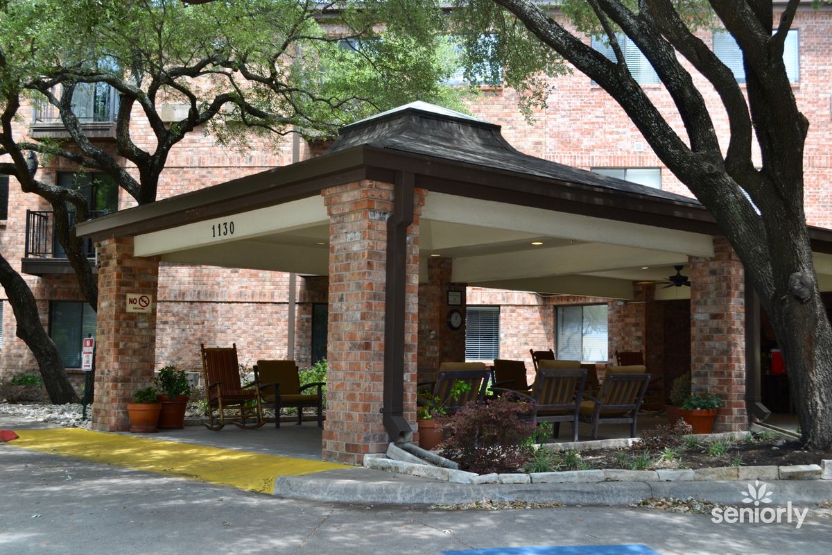 A building entrance with a canopy, surrounded by trees and outdoor seating.