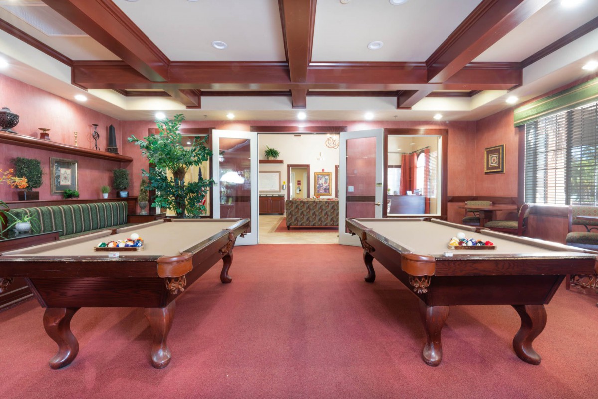 A stylish billiards room featuring two pool tables, wooden ceiling beams, and a red carpet for a luxurious ambiance.