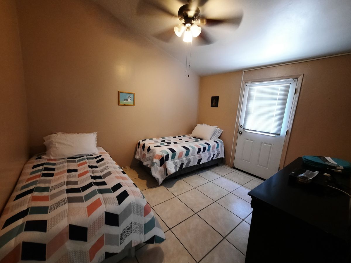A cozy bedroom with two single beds, a ceiling fan, and tiled flooring.