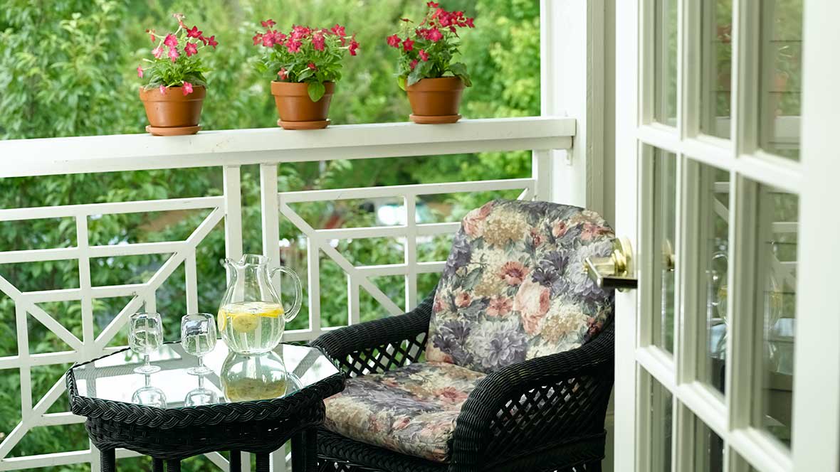 A cozy porch setup with a cushioned chair, table, and potted plants.