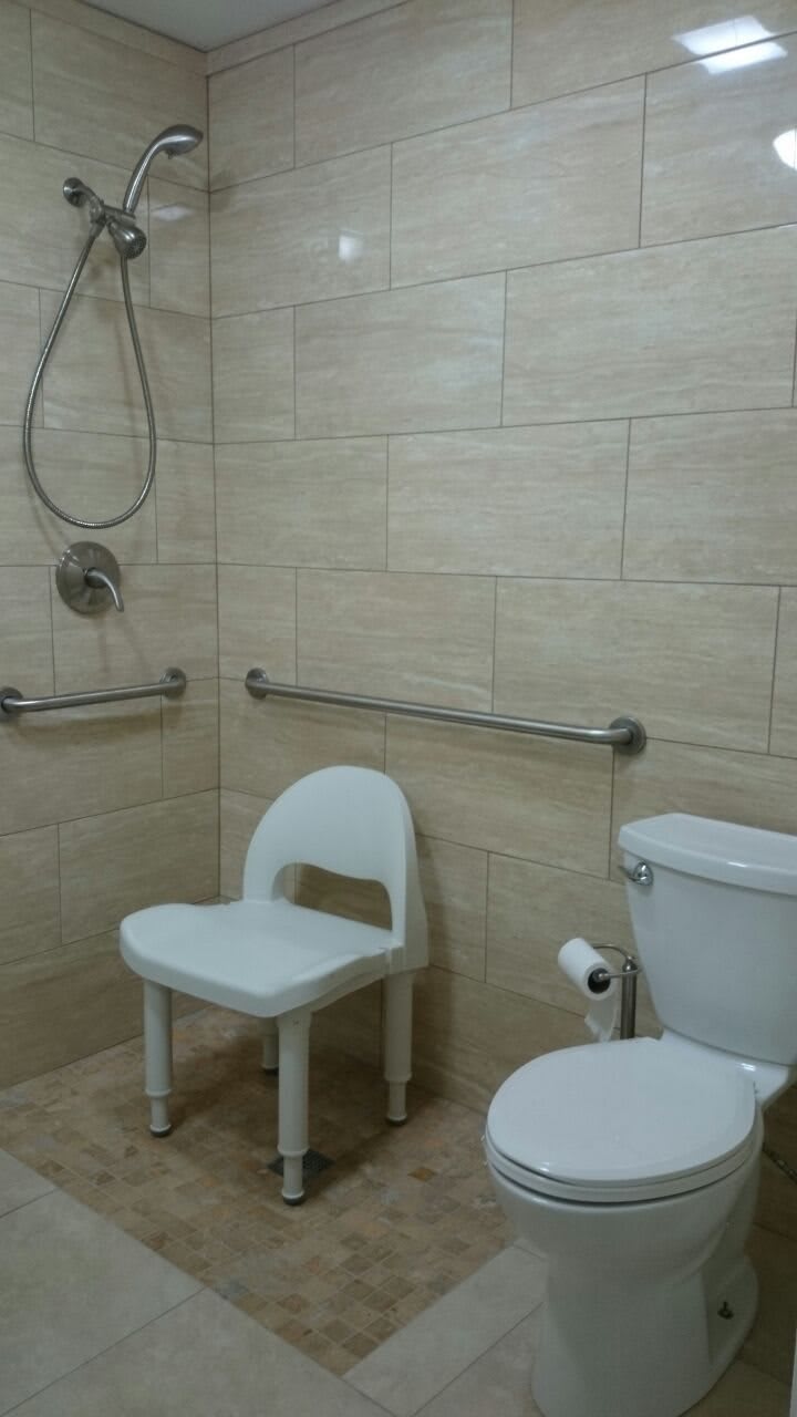 An accessible bathroom with a shower, grab bars, and a chair for seating.