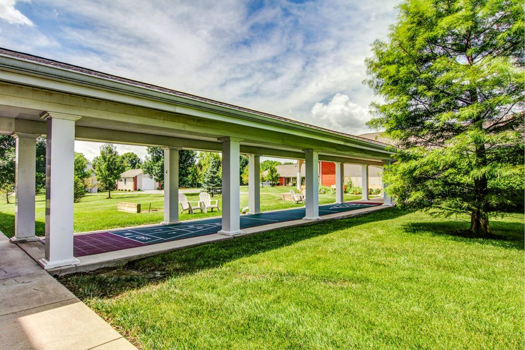 A covered walkway surrounded by lush green lawns and trees under a partly cloudy sky.