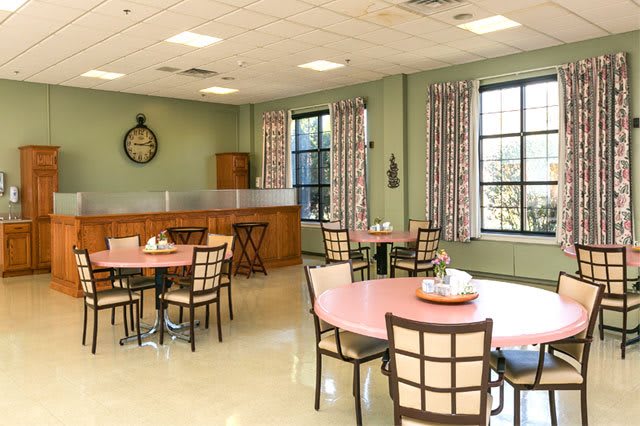 A well-lit dining area with multiple tables and chairs, featuring large windows and decorative curtains.