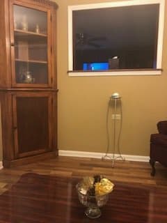 A cozy living room with a corner cabinet, window, and chair on wooden flooring.