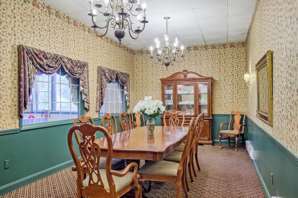 A traditional dining room with elegant wooden furniture, featuring a large dining table and chairs, chandeliers, and a china cabinet.