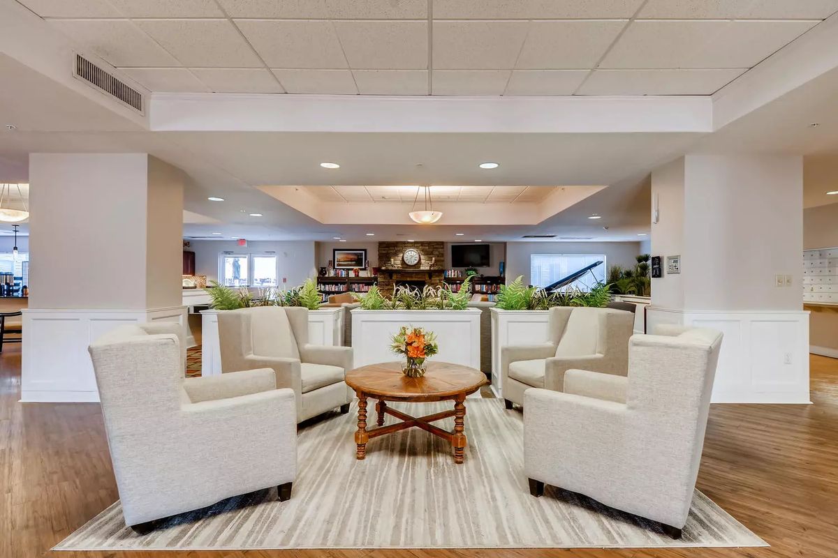 A modern hotel lobby with a comfortable seating area, featuring cream-colored chairs and a round wooden table adorned with flowers.