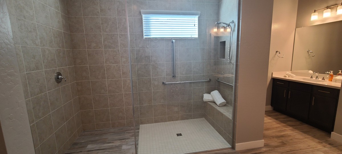 A modern bathroom with a glass-enclosed shower featuring tiled walls, a built-in bench, and safety grab bars.