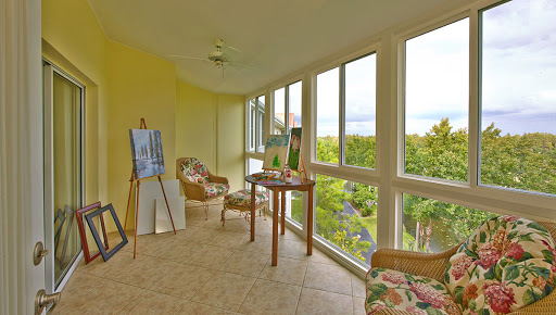 A bright and inviting sunroom featuring comfortable seating, art displays, and expansive windows offering a beautiful view of the outdoors.