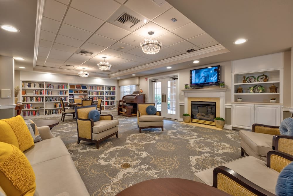 A cozy library with comfortable seating, bookshelves, a fireplace, and a piano.