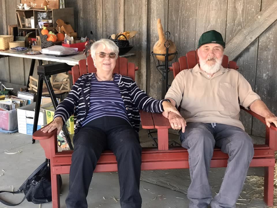An elderly couple sits on a bench, holding hands and relaxing on the patio.