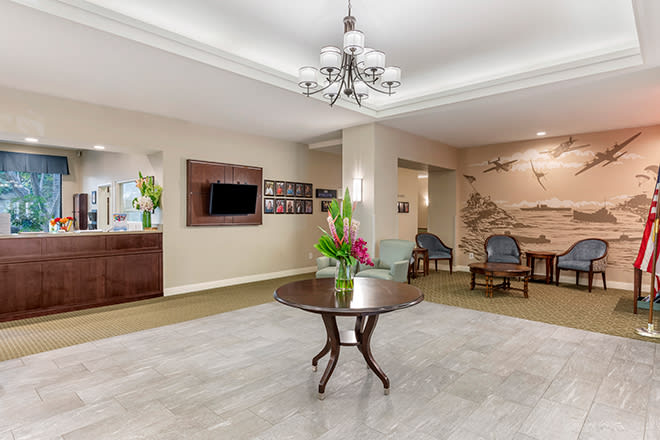 A welcoming lobby with a central table adorned with flowers, elegant chandelier lighting, and comfortable seating.