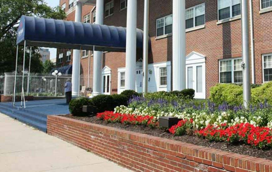 A building entrance with columns, landscaped flowers, and a brick pathway.