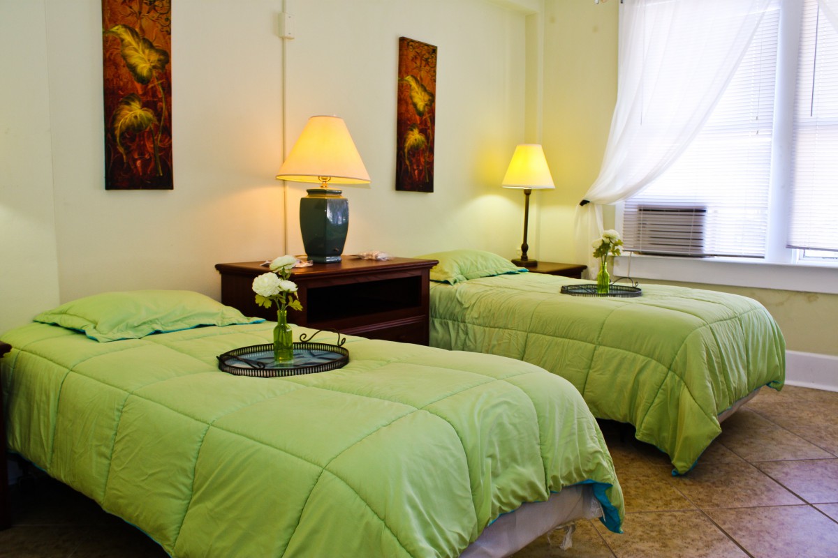 A cozy bedroom with twin beds featuring green bedding, illuminated by warm lamps and accented with floral decor.