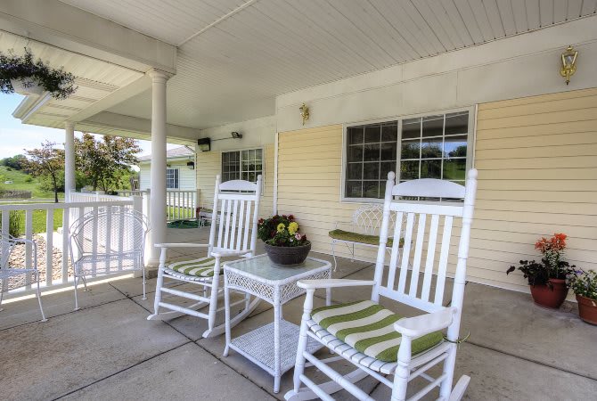 A cozy porch with white rocking chairs and a small table with flowers, perfect for relaxing on a summer day.